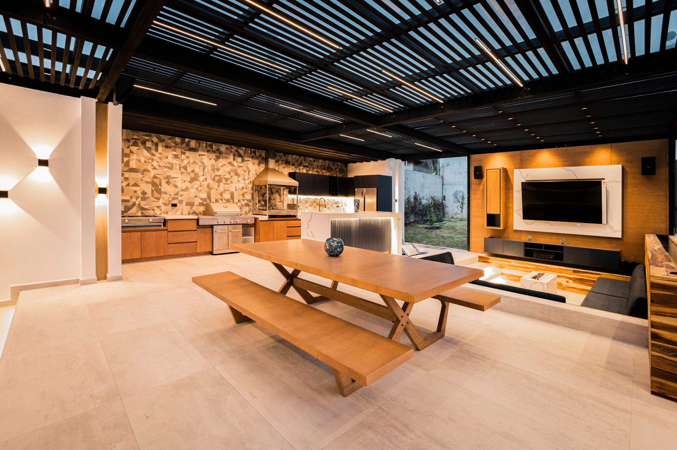 Modern outdoor living space with a sleek kitchen, seating area, wood accents, and mounted television